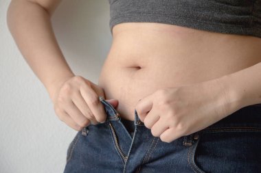 Kot giyen şişman bir kadın. Elleri kalçasında kilo aldığı için pantolonu kapatamıyor. Diyet konsepti.