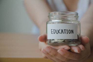 Kadın, gelecekte eğitim için cam kavanoz bursu biriktiriyor. Ahşap masa, klasik, minimal..
