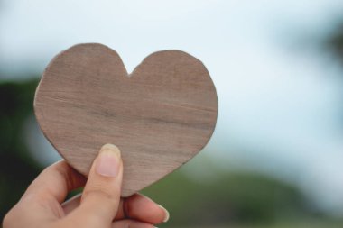 Bulanık yeşil arka planda ahşap kalbi tutmak, sevgililer günü konseptini sevmek.