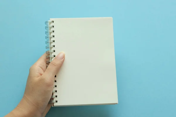 Mano Sosteniendo Cuaderno Blanco Sobre Fondo Azul —  Fotos de Stock