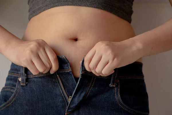 Fat woman wearing jeans.Hands unable to close the pants due to gaining fat on hips.Diet concept