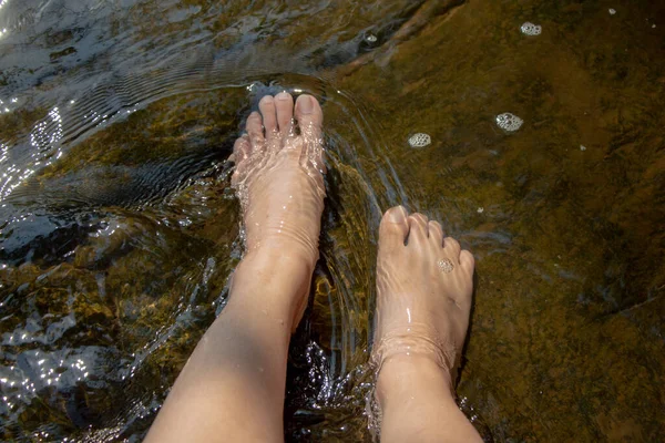 Woman relaxing.Dipping feet in water with rock at the background.