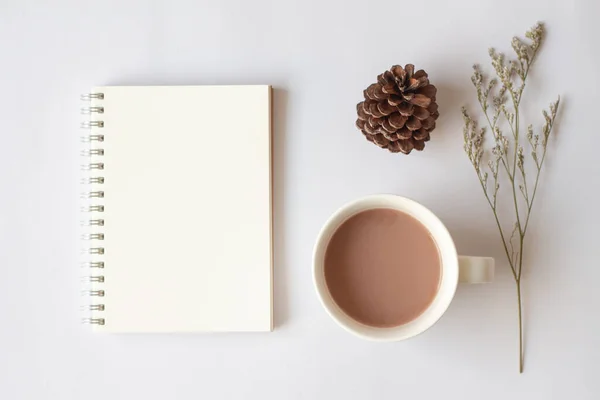 Kağıt defter, kalem, bir fincan kahve, kozalak ve beyaz arka planda kuru çiçekler. Ofis masaüstü görünümü. En düşük biçim.