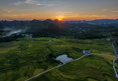 Dushan İlçesi, Qiannan Bölgesi, Guizhou, Çin 'deki karst kırsal tepeli küme arazisinde dağ zirveleri ile iç içe geçmiş pirinç tarlaları yer alıyor..