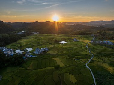 Dushan İlçesi, Qiannan Bölgesi, Guizhou, Çin 'deki karst kırsal tepeli küme arazisinde dağ zirveleri ile iç içe geçmiş pirinç tarlaları yer alıyor..