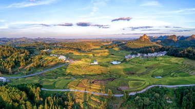 Dushan İlçesi, Qiannan Bölgesi, Guizhou, Çin 'deki karst kırsal tepeli küme arazisinde dağ zirveleri ile iç içe geçmiş pirinç tarlaları yer alıyor..