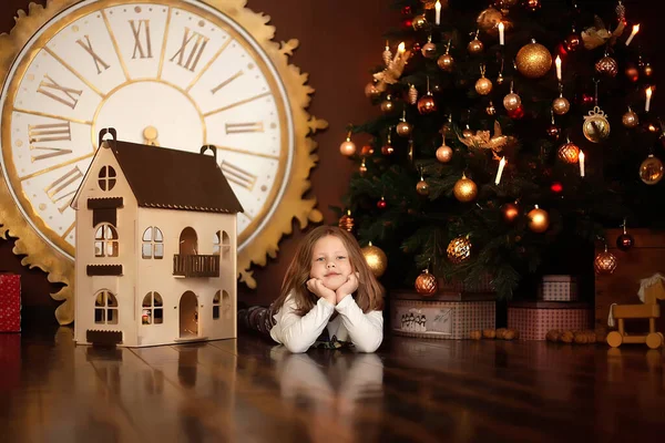 小さな美しい女の子横にクリスマスの新年の木とギフトと人形の家 — ストック写真