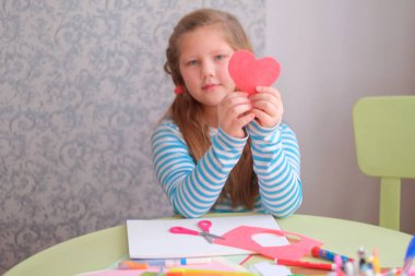 Bir kız çocuğu resim çizer, resim yapar, bir kalp çıkarır. Kalbi olan bir kızın portresi. Çocukların yaratıcılığı. Sevgililer Günü için hediye, Anneler Günü, Babalar Günü. Evde karantina sırasındaki dersler.