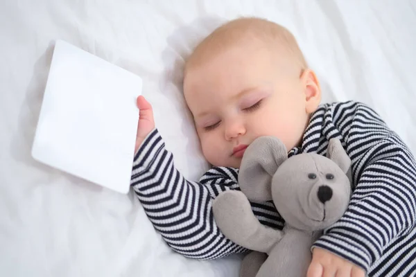 一个睡着的婴儿 手里拿着一张白色卡片 手里拿着一只心爱的软玩具老鼠 文字的位置 复制空间 穿着条纹睡衣的孩子特写 选择性聚焦 — 图库照片