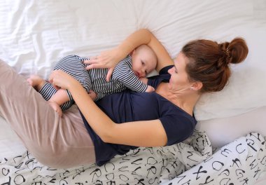 Anne bebekle birlikte yatakta yatıyor, bebeği emziriyor, yatağına yatırıyor. Çizgili pijamalı çocuk, sürekli emziriyor.