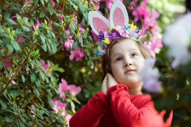 Tavşan kulaklı şirin kız Paskalya günü açelya bahçesinde yumurta avına katılıyor.