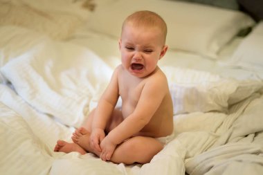 Aile hayatı vurulması. Seçici odaklanma. Sıcak dergi tonu, eklenen sesler. Uyanmış bebek yatağa bebek beziyle oturur ve ağlar.