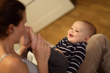 Aile hayatı vurulması. Seçici odaklanma. Sıcak dergi tonu, fazladan ses. Anne bebekle oynar - bebeğin ayaklarını öper - çocuk güler