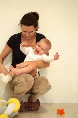 Aile hayatı vurulması. Seçici odaklanma. Sıcak dergi tonu, fazladan ses. Annem kaprisli ve mücadele eden bebeğe çorap giyer. Bir çocuğu kaprisle giydirmek