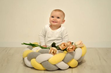 Aile hayatı vurulması. Seçici odaklanma. Sıcak dergi tonu, biraz da gürültü. Çocuk yastığa oturur ve çiçeklerle oynar.