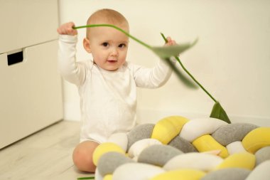 Aile hayatı vurulması. Seçici odaklanma. Sıcak dergi tonu, biraz da gürültü. Çocuk yastığa oturur ve çiçeklerle oynar.