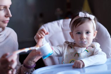 Annem sandalyedeki bebeği kaşıkla besliyordu. Kameraya bakan bir kız. Aile tarzı çekim. Seçici odak. 