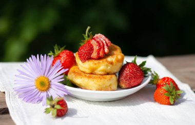 Beautiful summer breakfast - cheesecakes pancakes syrniki with fresh strawberries on a white plate. Tea in a tnka porcelain cup, sun glare and shadows. Linen tablecloth, rustic style, provence
