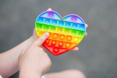 Colorful antistress sensory toy fidget push pop it in kid's hands. Modern toy simple dimple in the shape of a heart