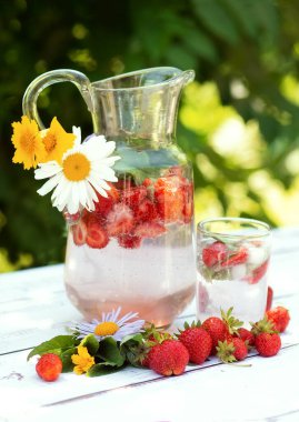 Beyaz ahşap bir kırsal masada cam bir sürahide ev yapımı çilekli mojito limonata. Çilek, nane filizleri ve çiçekler. Soğuk yaz içeceği. Dikey.