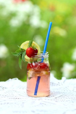 Ev yapımı soğuk çilekli mojito limonata, cam kavanozda, masada mavi pipetle yaz bahçesinde beyaz örülü masa örtüsü. Boş zamanlarında ev yapımı meşrubat.