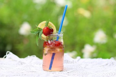 Ev yapımı soğuk çilekli mojito limonata, cam kavanozda, masada mavi pipetle yaz bahçesinde beyaz örülü masa örtüsü. Boş zamanlarında ev yapımı meşrubat.