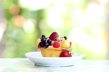 Kremalı ve çilekli kek turtası - ahududu, çilek, frenk üzümü, kiraz, bahçedeki masada beyaz bir tabakta.