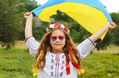 Ukrayna 'nın sarı ve mavi bayrağı nakışlı gömlekli güzel bir kızın ellerinde ve kurdeleli bir çelenk. Buğday tarlasında bir çocuk. Ukrayna 'nın Bağımsızlık Günü, Bayrak, Anayasa, Nakış. Pankart