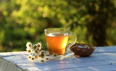 Tahta bir masada bir fincan papatya çayı. Şeffaf bir fincanda papatya çayı ve ahşap masada papatya çiçeği. Bebeğin midesi için bitki çayı. Boşluğu kopyala.