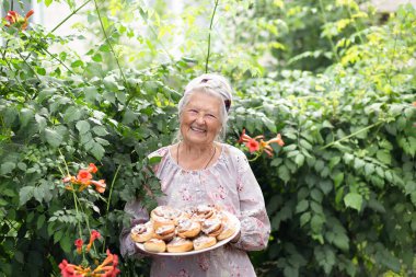 Yaşlı, mutlu, gri saçlı, mutlu bir büyükannenin ellerinde çörekler. Büyükanne tarçınlı çörek pişirir ve kurabiye pişirir. Portre, seçici odaklanma
