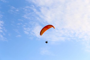 Turuncu paraglider bulutların arka planında mavi gökyüzünde uçuyor. Güneşli bir günde gökyüzünde paraşütle atlamak.