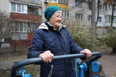 Elderly woman exercising outdoors using public gym equipment, promoting healthy aging and active lifestyle