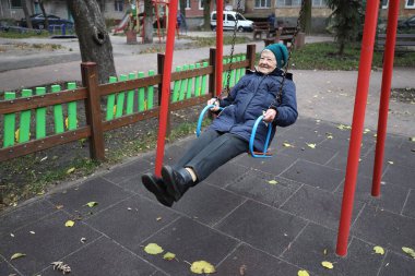 Mutlu aktif 90 yaşındaki yaşlı kadın parkta salıncakta sallanırken eğleniyor.