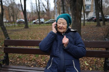 Yaşlı bir bayan bir sonbahar günü parkta yürür, doğanın tadını çıkarır, telefonda konuşur.
