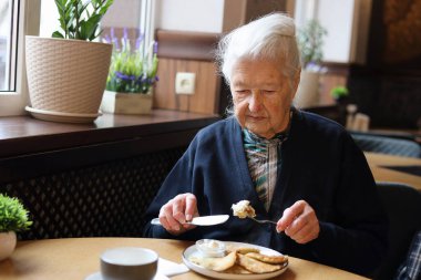 Restoranda yemek yiyen 90 yaşında, kır saçlı, son sınıf öğrencisi bir kadının portresi. Çorba, ana yemek, çay. Konuşma.