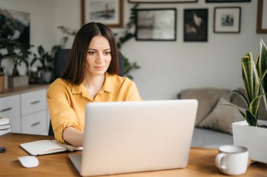 Evde bilgisayarla çalışan mutlu ve serbest bir genç kadın. Çevrimiçi öğrenim gören çekici iş kadını, dizüstü bilgisayar, web sörfü bilgileri veya internet mağazasından alışveriş yapıyor..