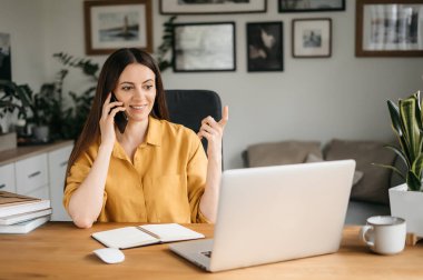 Gülümseyen bir iş kadını cep telefonuyla konuşur ve evde çalışırken dizüstü bilgisayar kullanır, ekrana bakar, bir mesaj okur, genç bir bayan çalışana tavsiyelerde bulunur, telefon konuşmaları...
