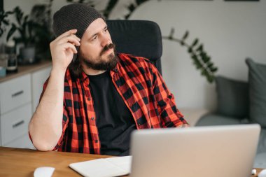 Odaklanmış sakallı genç adam, günlük giysiler içinde dizüstü bilgisayar kullanıyor, klavyeye yazıyor, e-posta ya da mesaj yazıyor, sohbet ediyor, alışveriş yapıyor, bilgisayar üzerinde çalışan başarılı bir serbest yazar. 