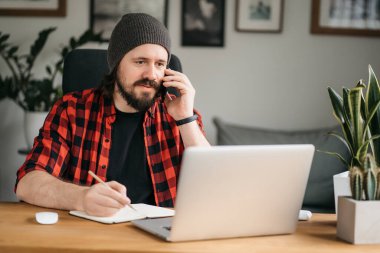 Odaklanmış sakallı genç adam, günlük giysiler içinde dizüstü bilgisayar kullanıyor, klavyeye yazıyor, e-posta ya da mesaj yazıyor, sohbet ediyor, alışveriş yapıyor, bilgisayar üzerinde çalışan başarılı bir serbest yazar. 