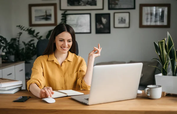Mooie jonge vrouw in casual dragen met behulp van laptop tijdens het werken binnen. Freelancer neemt deel aan een videoconferentie — Stockfoto