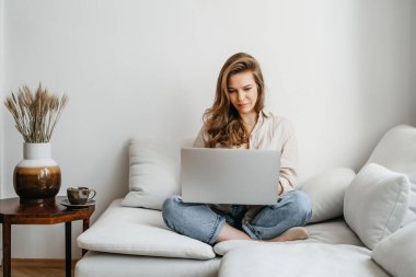 Kanepede oturup proje üzerinde çalışan, dizüstü bilgisayarda film izleyen, çalışan, blog yazan, dinlenen ve sohbet eden genç ve mutlu bir kadın serbest yazar portresi.