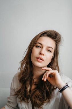 Genç bayan oturma odasındaki kanepede oturuyor. Beyaz rahat ev kıyafetleri içinde güzel bir sarışın.