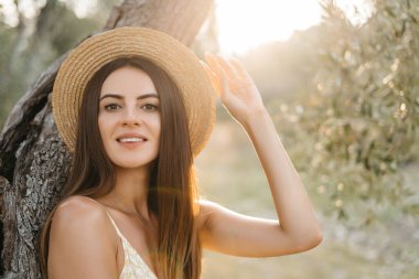 Zeytin bahçesinde gün batımında hasır şapkalı güzel esmer kadın portresi. İtalya 'ya seyahat, yaz tatili.