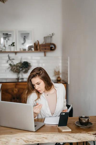 Een jonge vrouw maakt aantekeningen voor de laptop thuis. Werken vanuit huis. Begrip onderwijs en communicatie. — Stockfoto