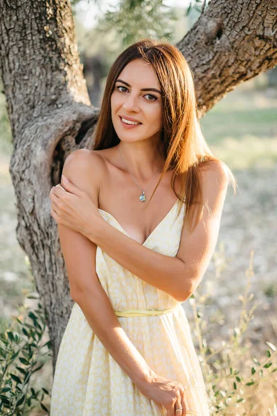 Een teder portret van een mooie brunette in mooi zonlicht. Vrouw in gele zomer linnen jurk in olijfboomgaard tuin. Natuurschoon.Reis naar Italië, zomervakantie — Stockfoto