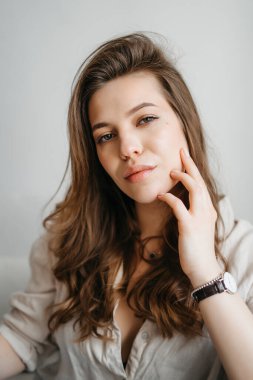 Genç bayan oturma odasındaki kanepede oturuyor. Beyaz rahat ev kıyafetleri içinde güzel bir sarışın.