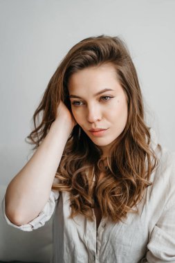 Genç bayan oturma odasındaki kanepede oturuyor. Beyaz rahat ev kıyafetleri içinde güzel bir sarışın.