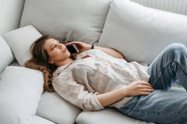 Genç kız telefonda konuşuyor, kanepede yatıyor.