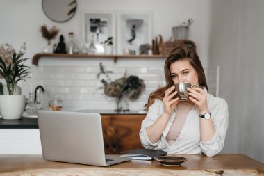 Bilgisayarla çalışan, kahve içen, evde çalışan, uzaktan eğitim alan gülümseyen bir kadın.