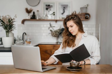 Genç bayan evde dizüstü bilgisayarın önünde notlar alıyor. Evden çalışıyorum. Eğitim ve iletişim kavramı.